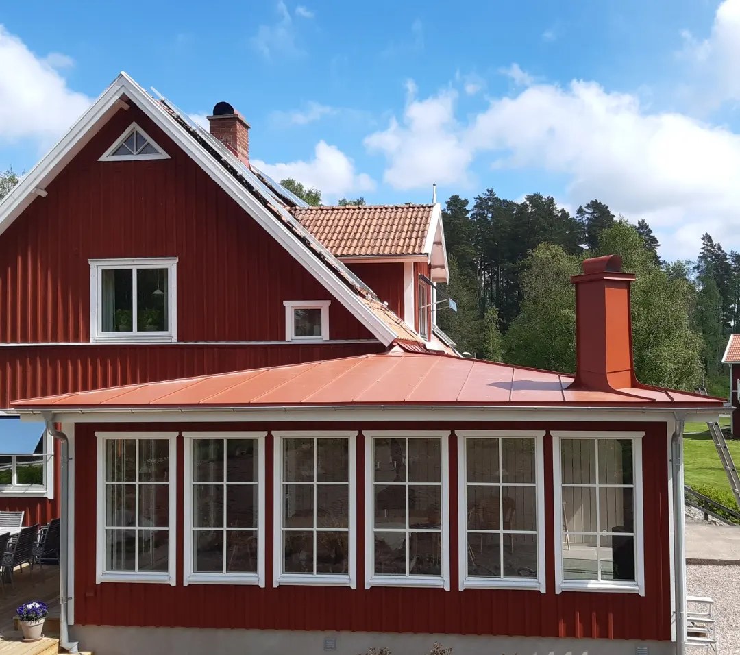 Röd villa med glasveranda, bandtäckt plåttak i tegelrött och helinklädd skorsten